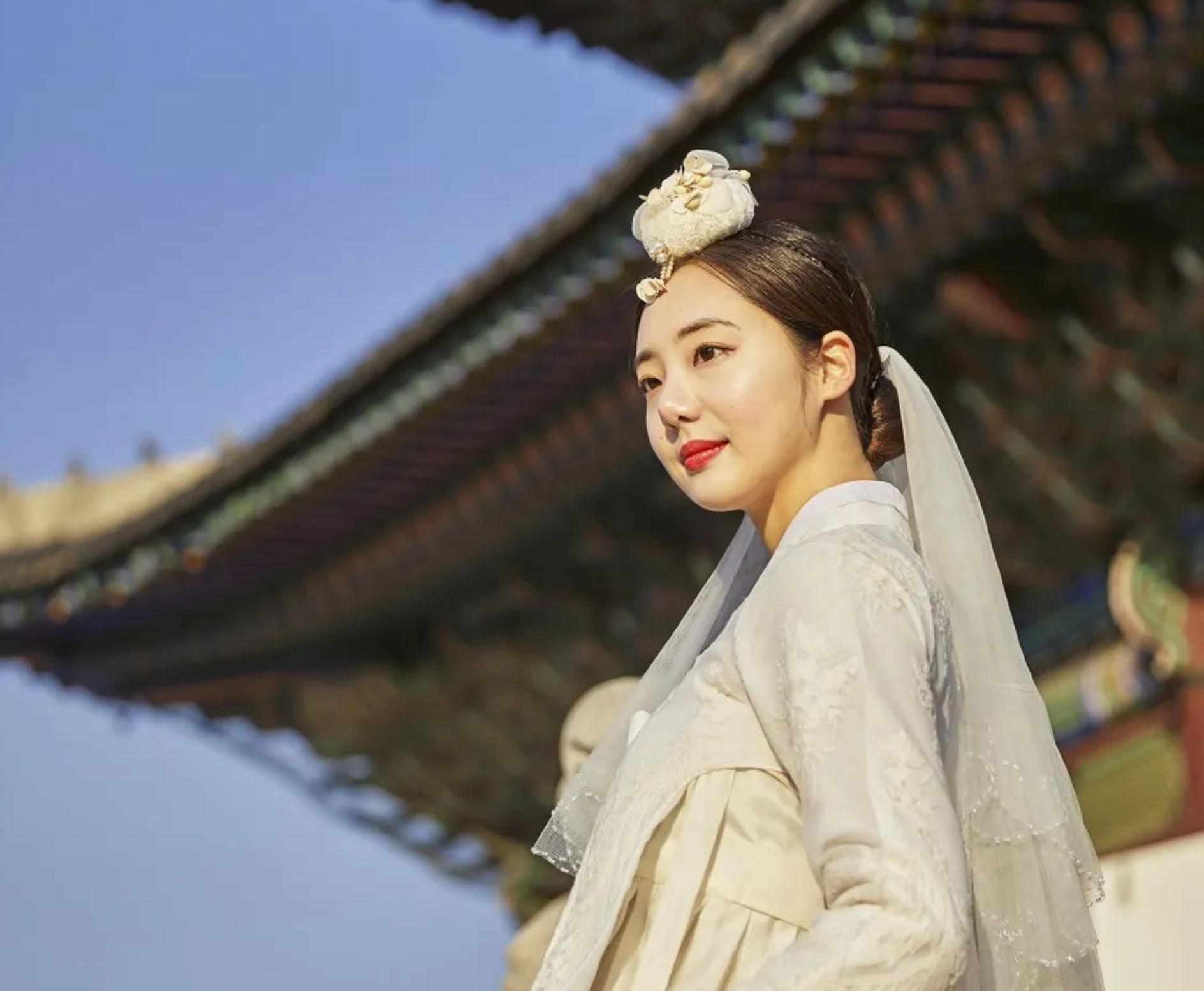 Happy woman wearing traditional Korean clothing, smiling against blue sky backdrop.