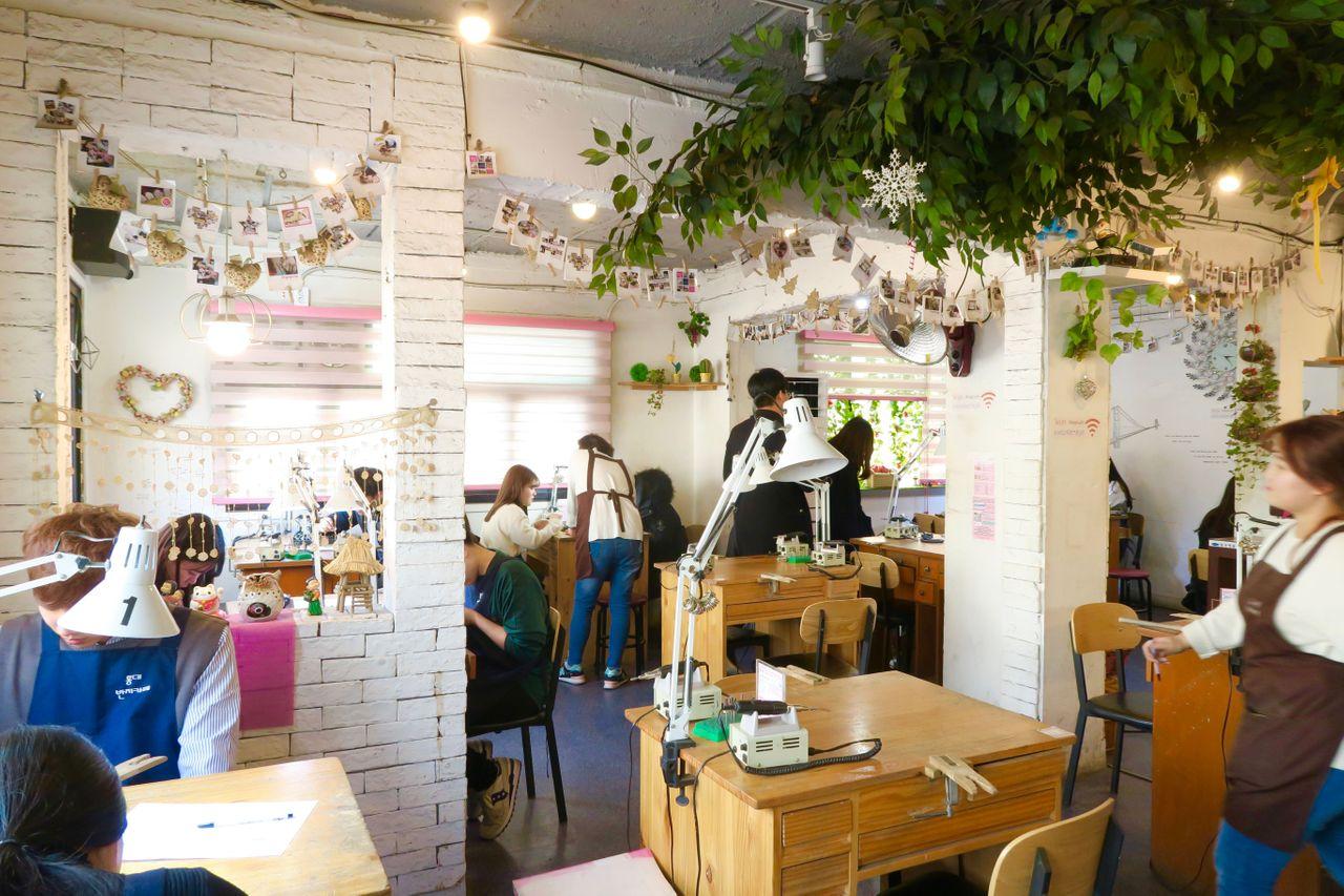 Interior view of a Hongdae jewelry-making cafe with tables, chairs and potted plants.