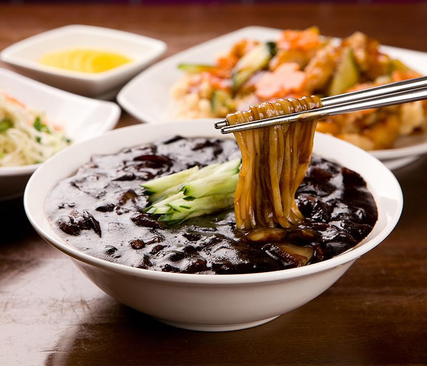 Jjajangmyeon with tableware and ingredients in a mixing bowl, a staple dish of Korean cuisine.