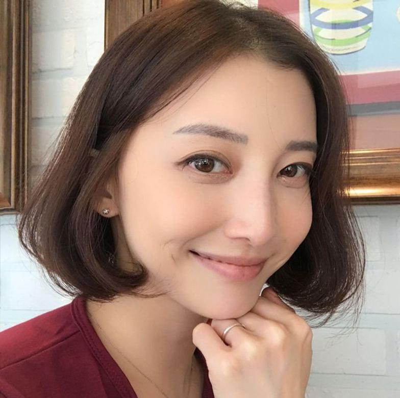 A woman with semi-permanent eyebrow tattoos and eyelash extensions smiles, highlighting her forehead, nose, cheek, skin, lips, chin, and flawless makeup.