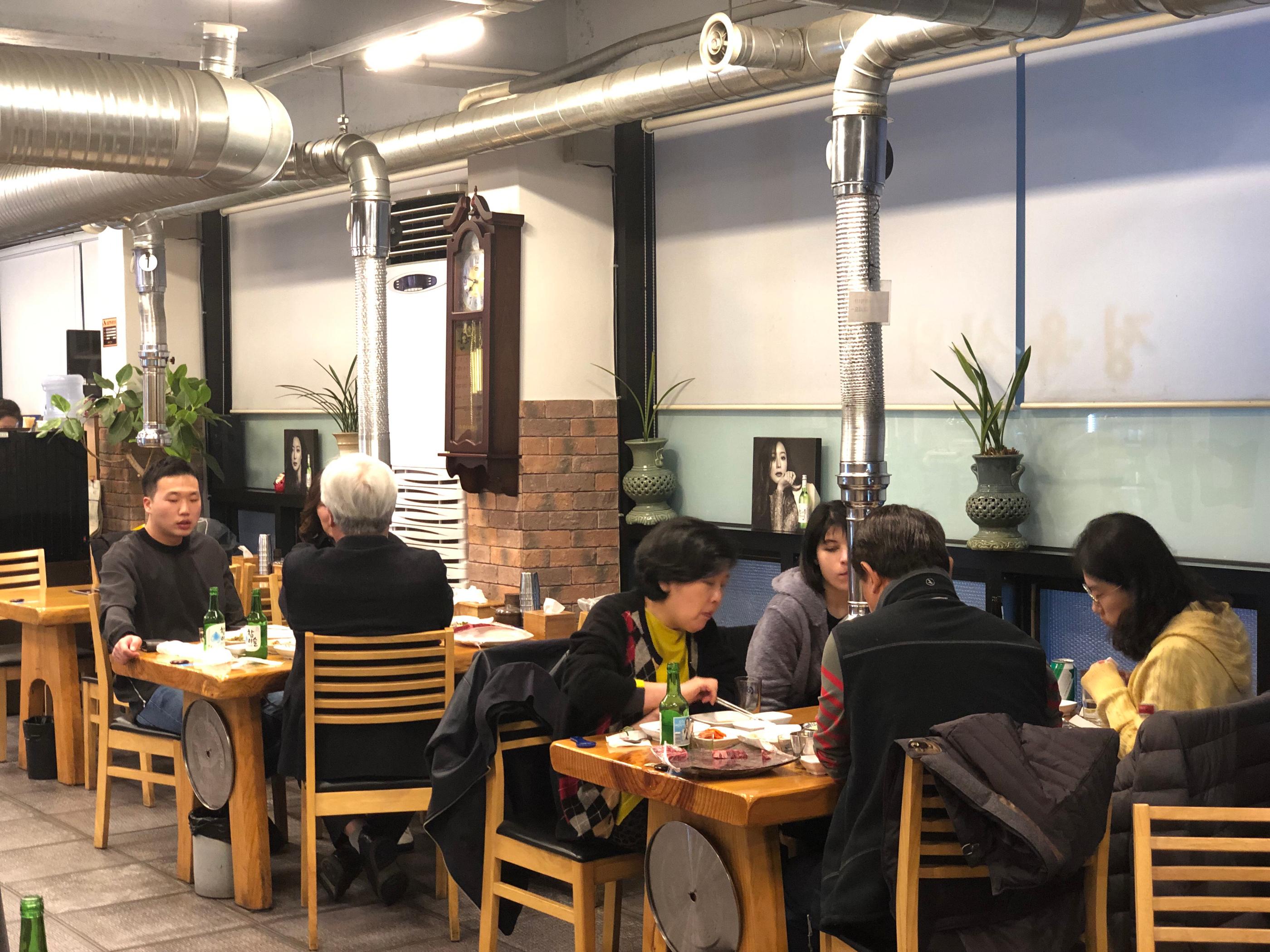 Interior of 마장골 restaurant in Korea, featuring wooden furniture, green plants, and elegant lighting.