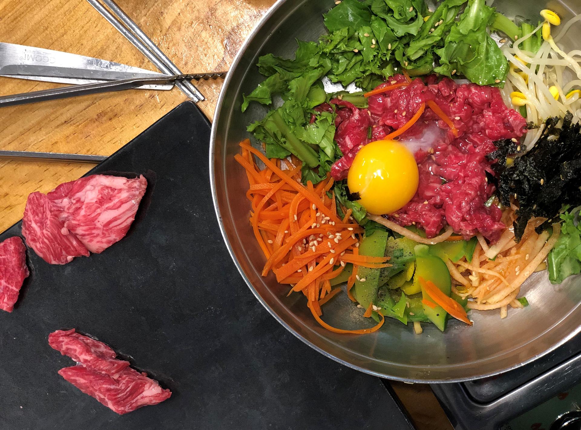 Traditional Korean bibimbap with marinated raw beef, vegetables, egg yolk, and rice served on tableware