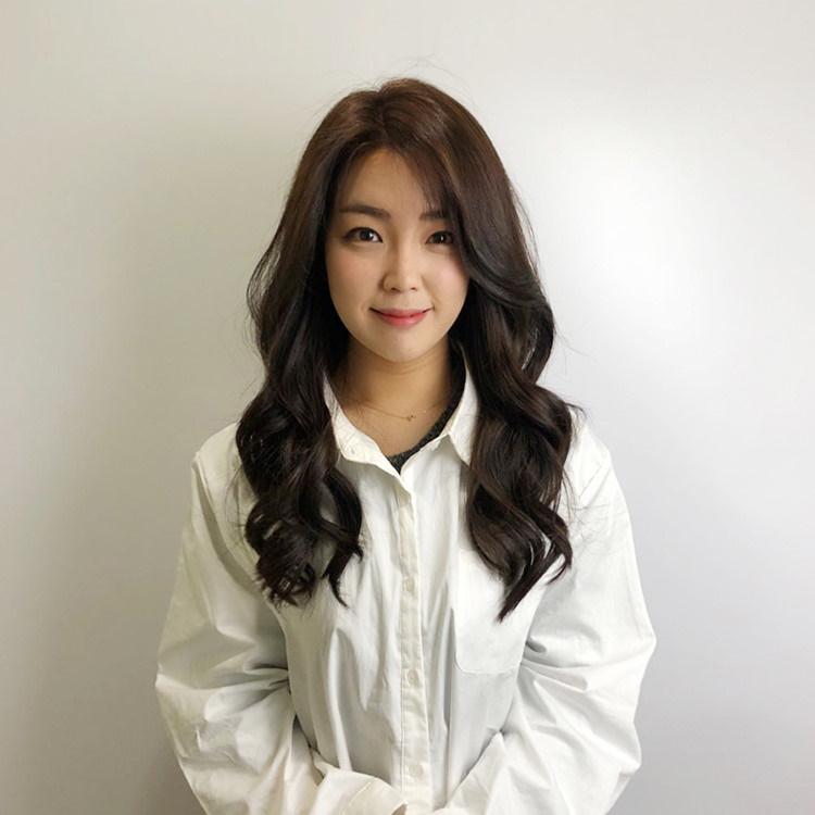 Model showcasing Juno Hair's latest styles at Centum City Station in Busan, wearing an elegant dress shirt and outerwear, with a focus on her face, hair, lips, and eyebrow.