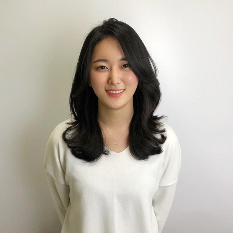 Smiling model with trendy hair and makeup, featuring eyebrows, eyes, and lips at Juno Hair in Centum City, Busan.
