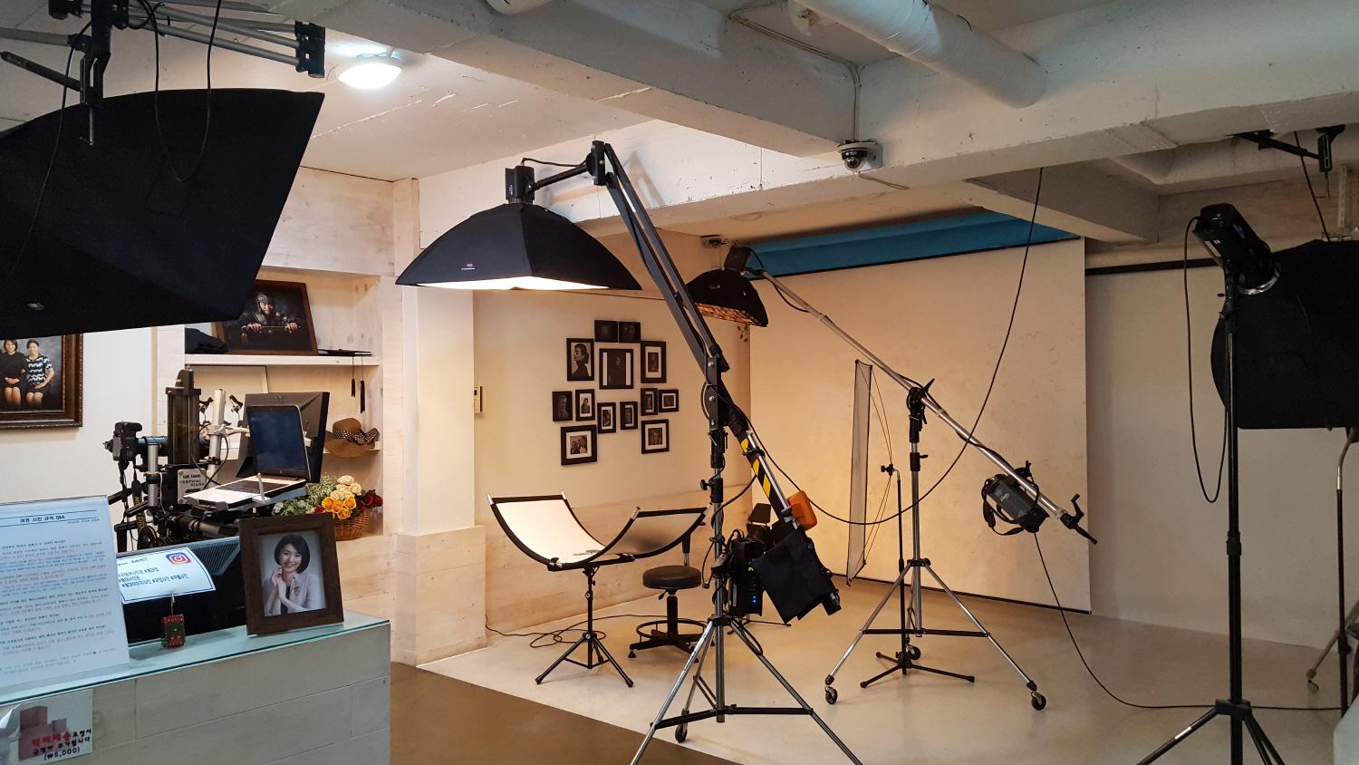 Interior of 우리동네사진관 Hongdae branch, showcasing film studio equipment, including tripods, microphone stands, and audio gear, under bright ceiling lamps.