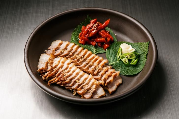 Plate of Korean pork belly and boiled pork, ready for delivery with side dishes and utensils on the table.