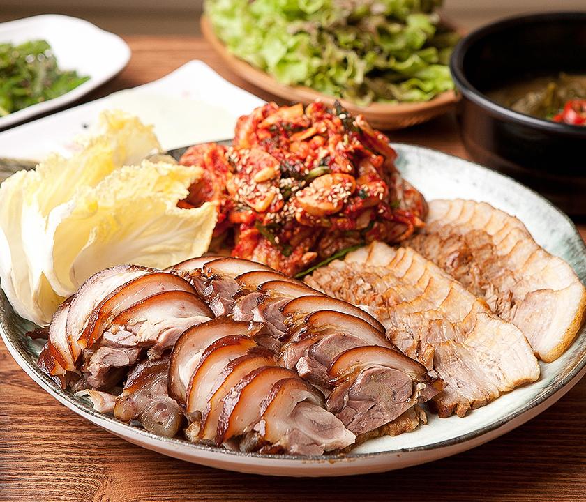 Delivery of Korean-style braised pork and boiled pork with seafood and vegetables on plates.