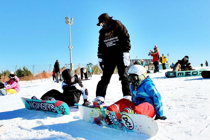 Instructor in dark jacket helps children in helmets sit on colorful snowboards on a sunny Eden Valley ski slope