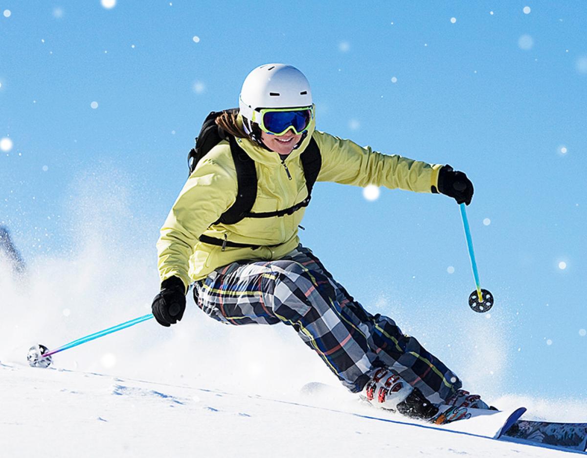 Woman in yellow jacket and plaid pants carving down snowy slope with ski poles at Eden Valley tour