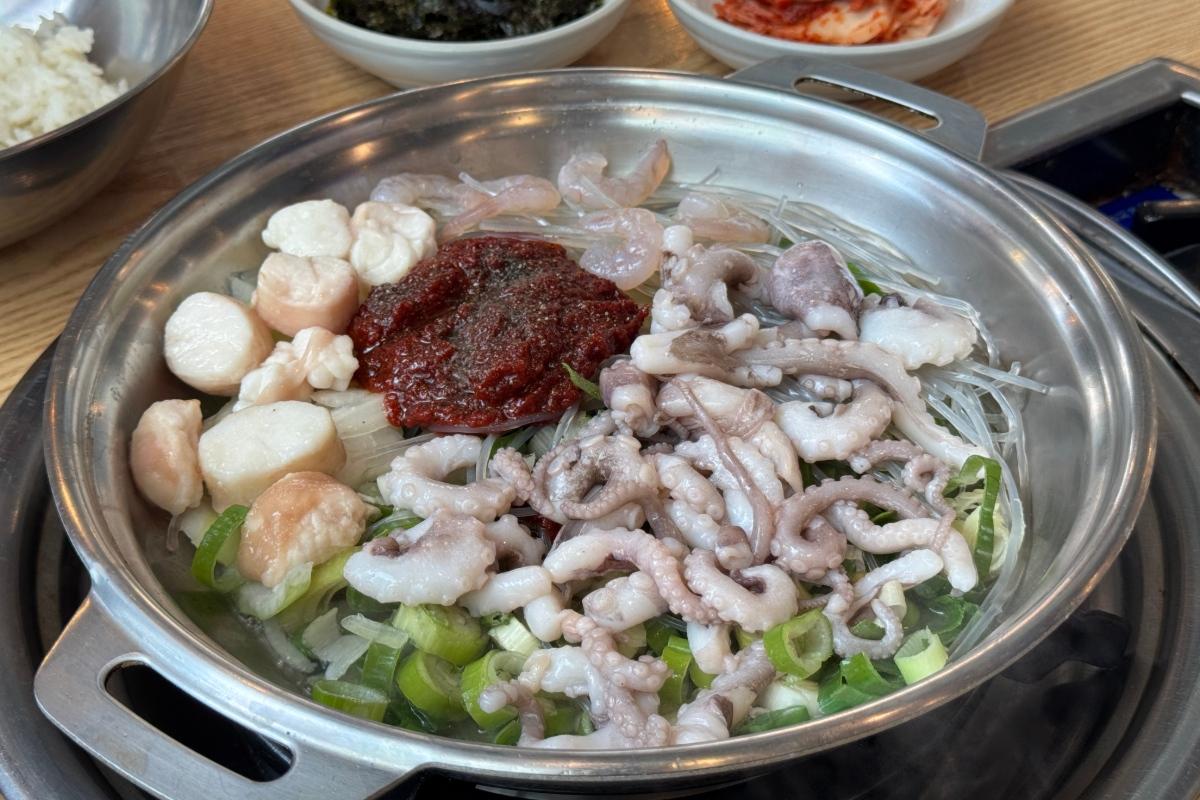 Century Octopus stainless pot of raw baby octopus, scallops, shrimp, glass noodles, green onions and red chili paste ready to cook