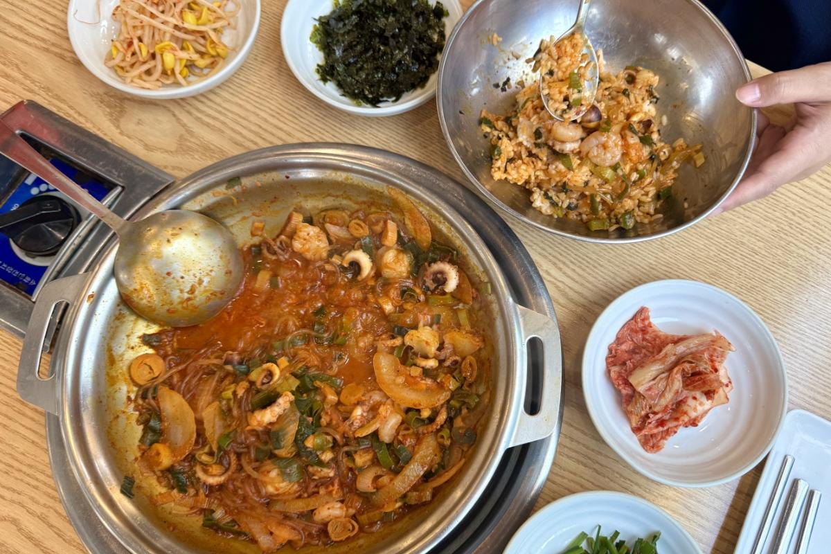Century Octopus spicy stir-fried octopus and vegetables in a metal pot with mixed rice, kimchi and side dishes on table