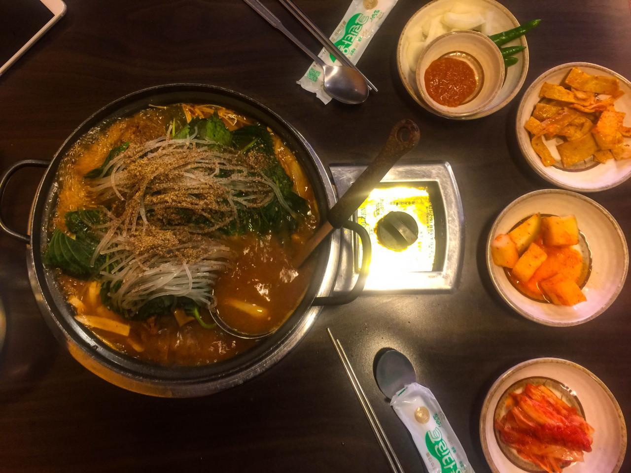 Sizzling hot 성균관 감자탕 dish on plate with traditional tableware and ingredients.