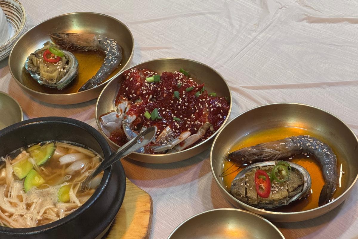 Brass bowls with soy-marinated raw crab, marinated prawn and abalone, and a bowl of clear soup with vegetables.