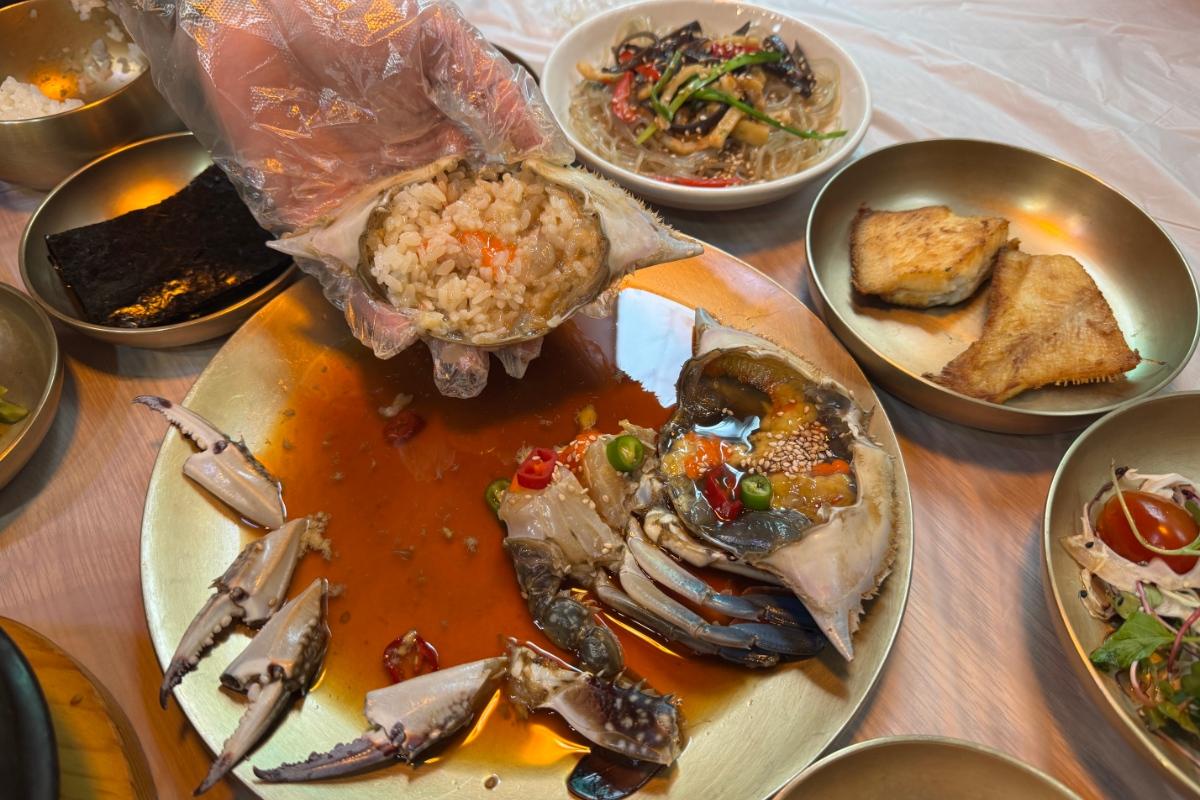 Soy-marinated raw crab served in shell with rice, chili and sesame on a gold plate surrounded by side dishes at Lee Ha Jung.