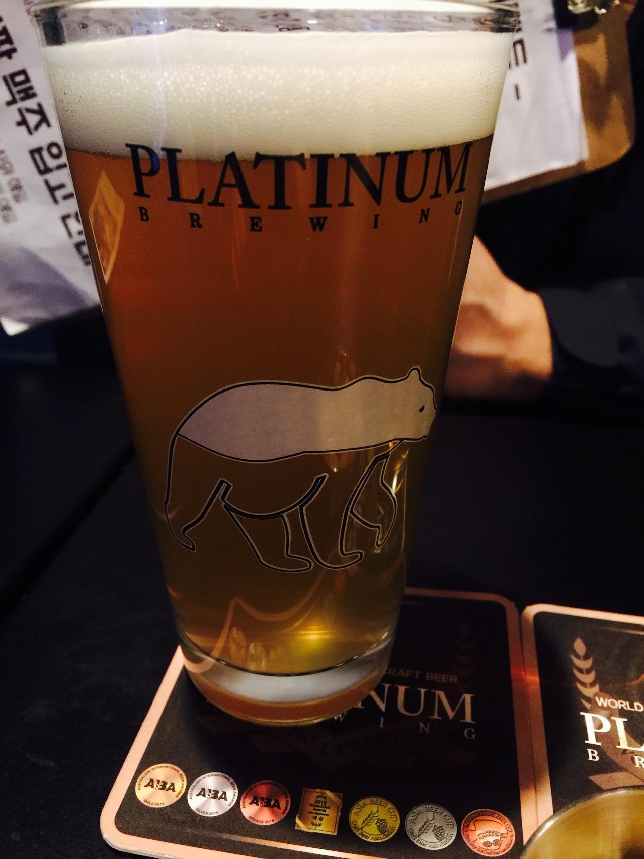 A foamy pint of beer in a bar setting, served in a clear glass with Liquid Lab branding.