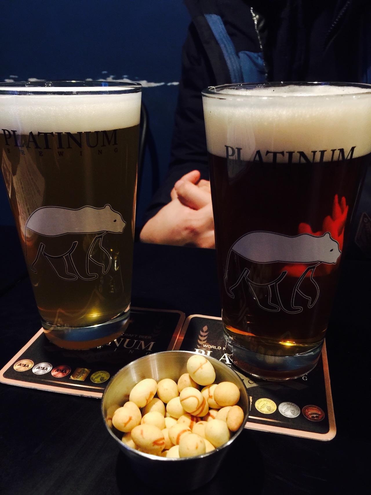 Beer glasses and tableware on a bar counter in a Korean pub, surrounded by food and drinks.