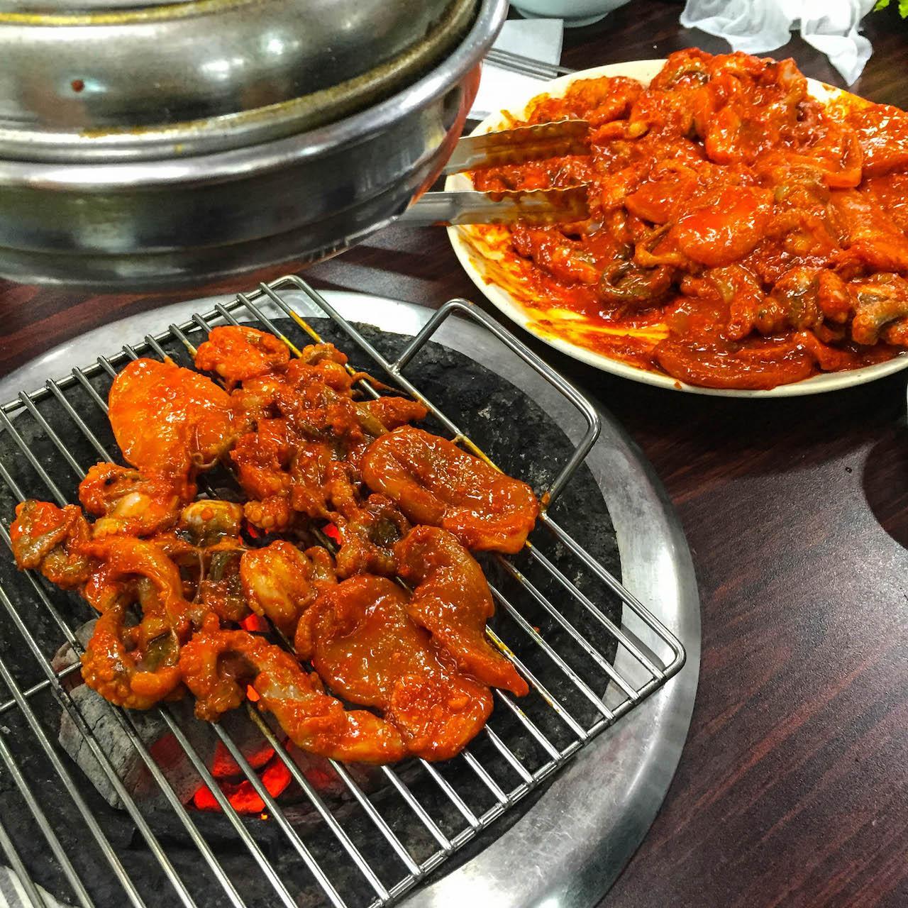grilled pork dish with spicy squid on an outdoor grill, served with tableware and ingredients.