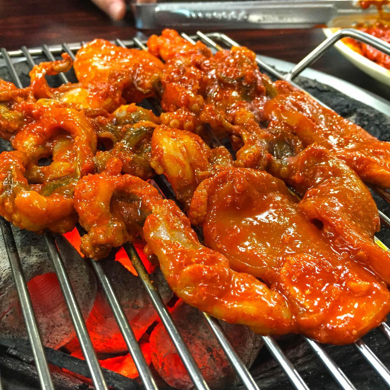 roasted spicy squid and pork belly on a table with Korean side dishes.