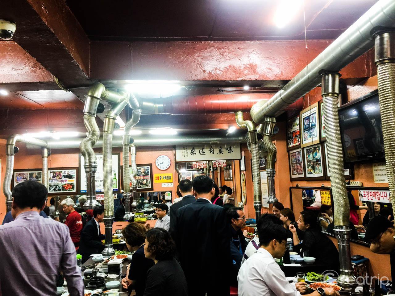 customers explore retail market selling various apparel like jackets, shirts, and t-shirts in a bustling city event featuring 충무로쭈꾸미불고기.