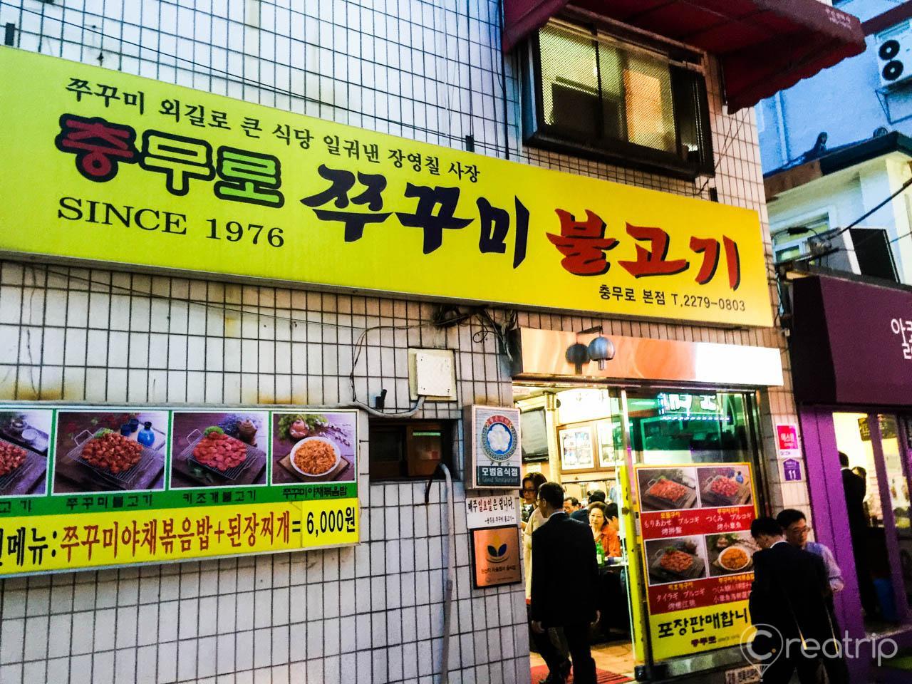 snapshot of yellow signage in the city with advertisement for Korean dish Chungmuro spicy squid bulgogi in retail storefront.