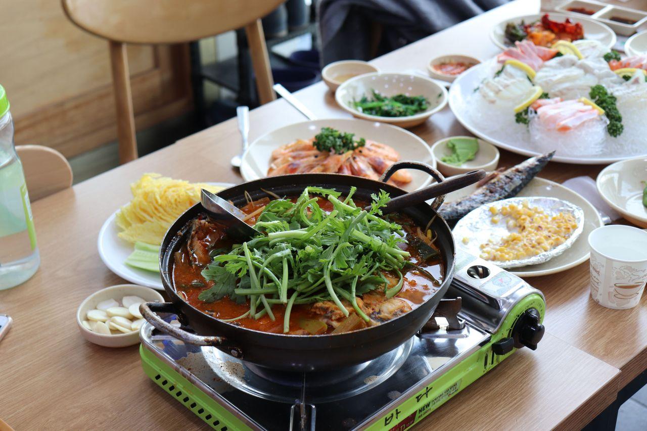 A table set with food from a seafood market in Seoul: spicy stew, Ching bo leung soup, and leafy greens.