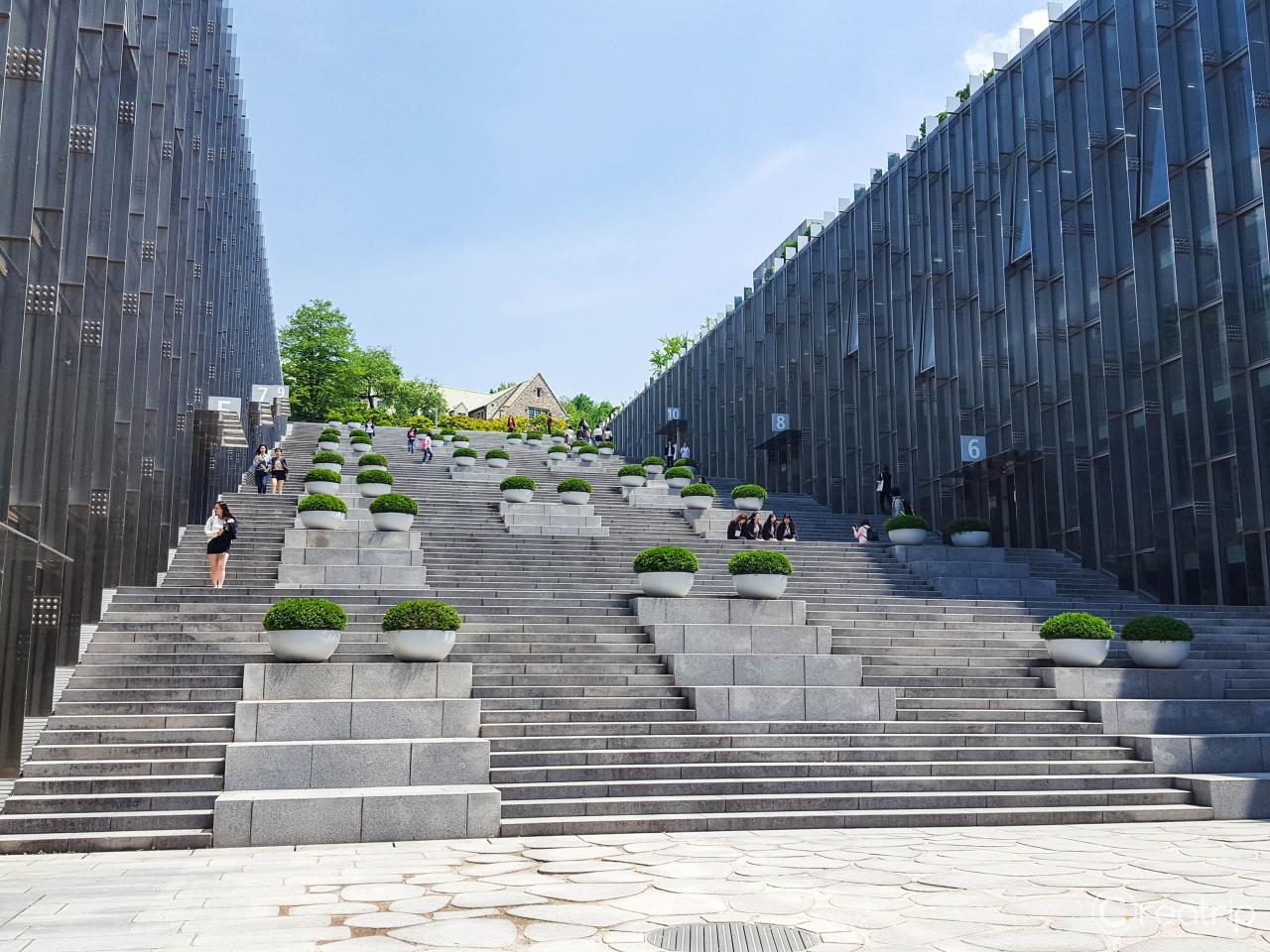 Ewha Womans University urban campus with skyscrapers, trees, and stairs under clouds.