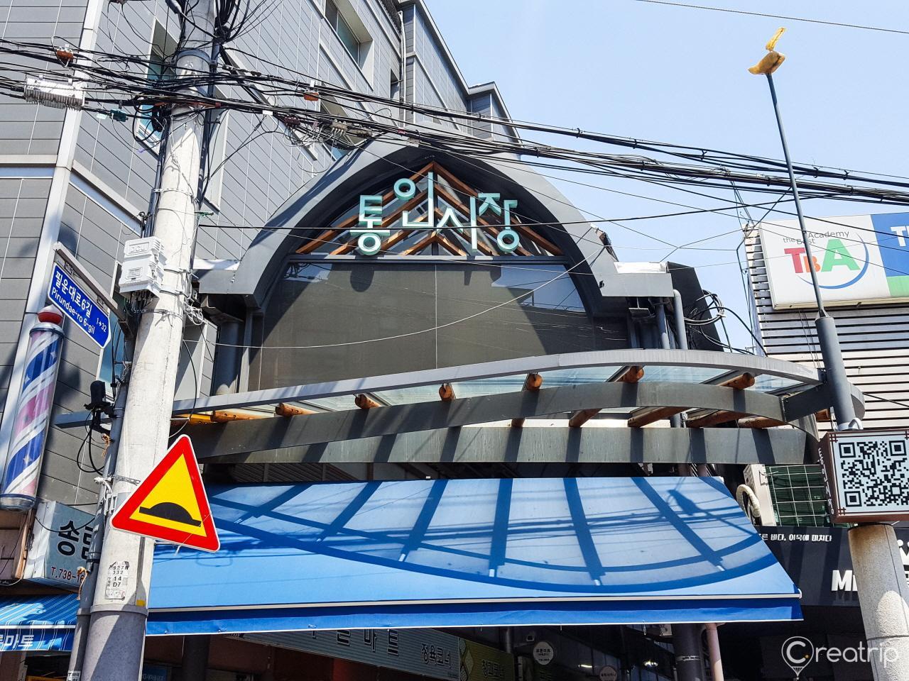 View of mixed-use building in cityscape, with vehicles and boats in foreground, and sky and window reflections in facade - location: 통인시장, Korea