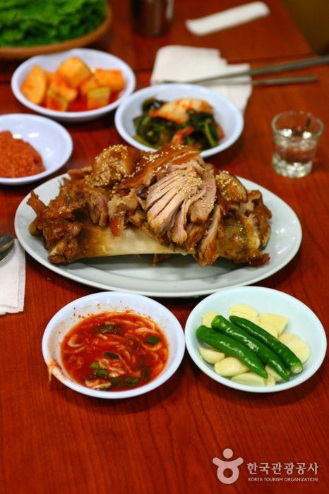 A dish of 공덕족발골목, a Korean cuisine of meat, vegetable, and herbs, on a plate with tableware.