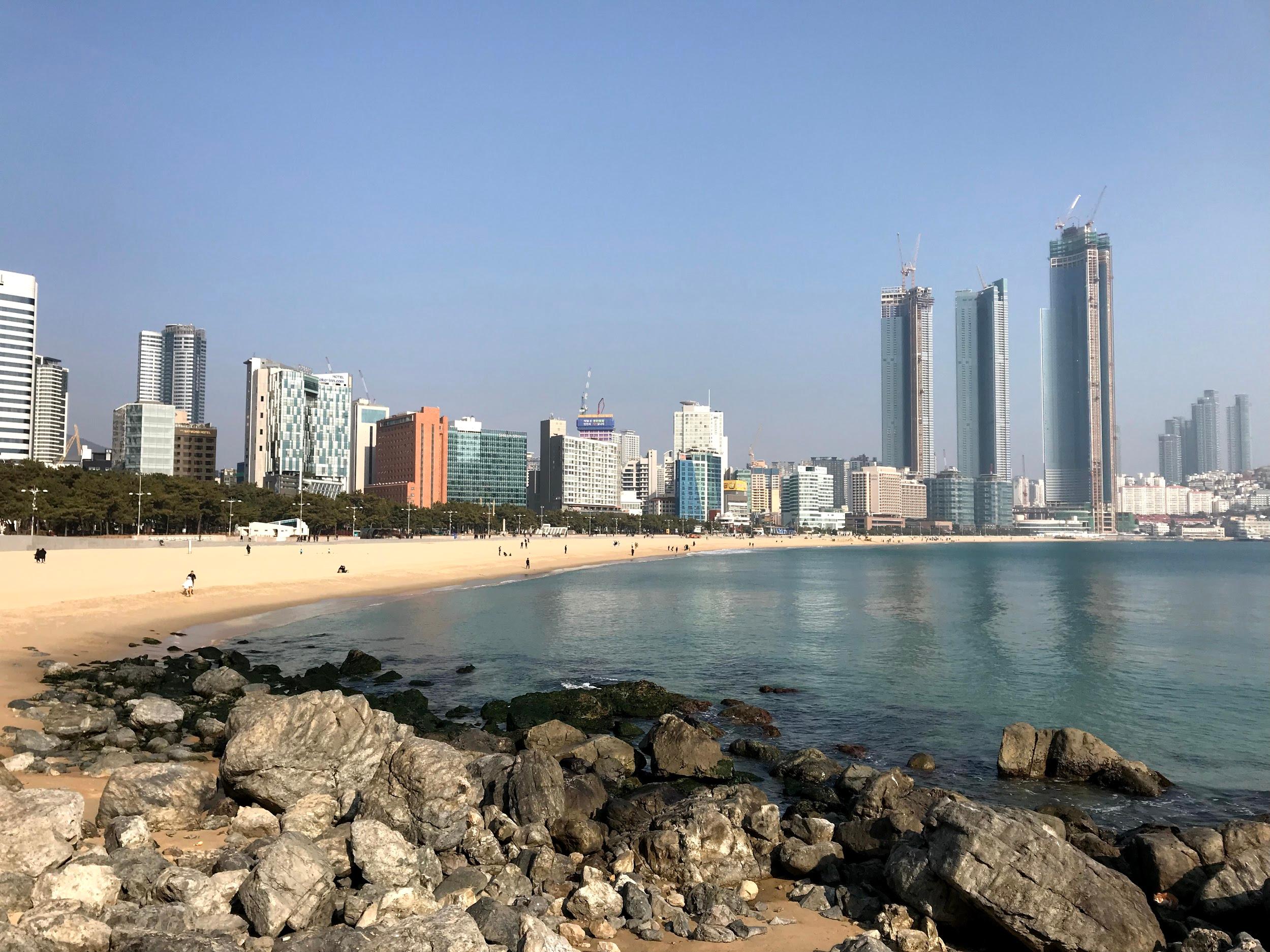 Aerial view of Busan cityscape with skyscrapers and condominiums. Water resources and the horizon meet the blue sky.