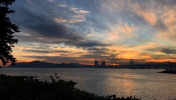 Sunlit trail on Dongbaek Island, Busan - natural landscape with clouds, sky, and water resources.