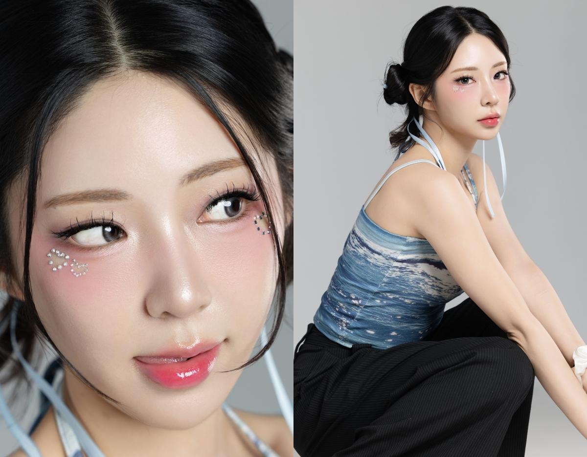 young woman with dark hair in low twisted buns, wearing blue ocean-patterned halter top and black pants, studio backdrop