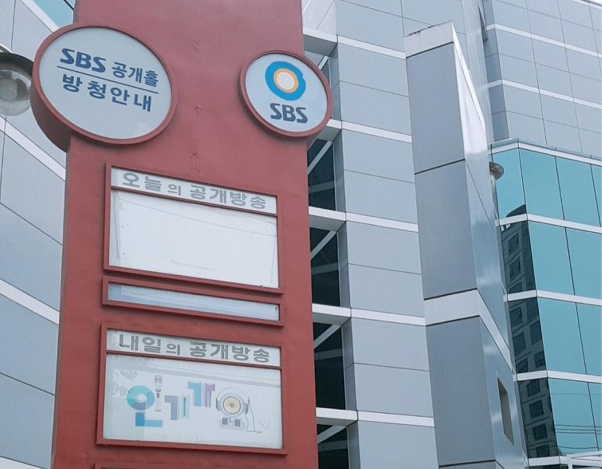 red vertical signboard with SBS logo and Korean text outside the modern SBS Deungchon Public Hall building