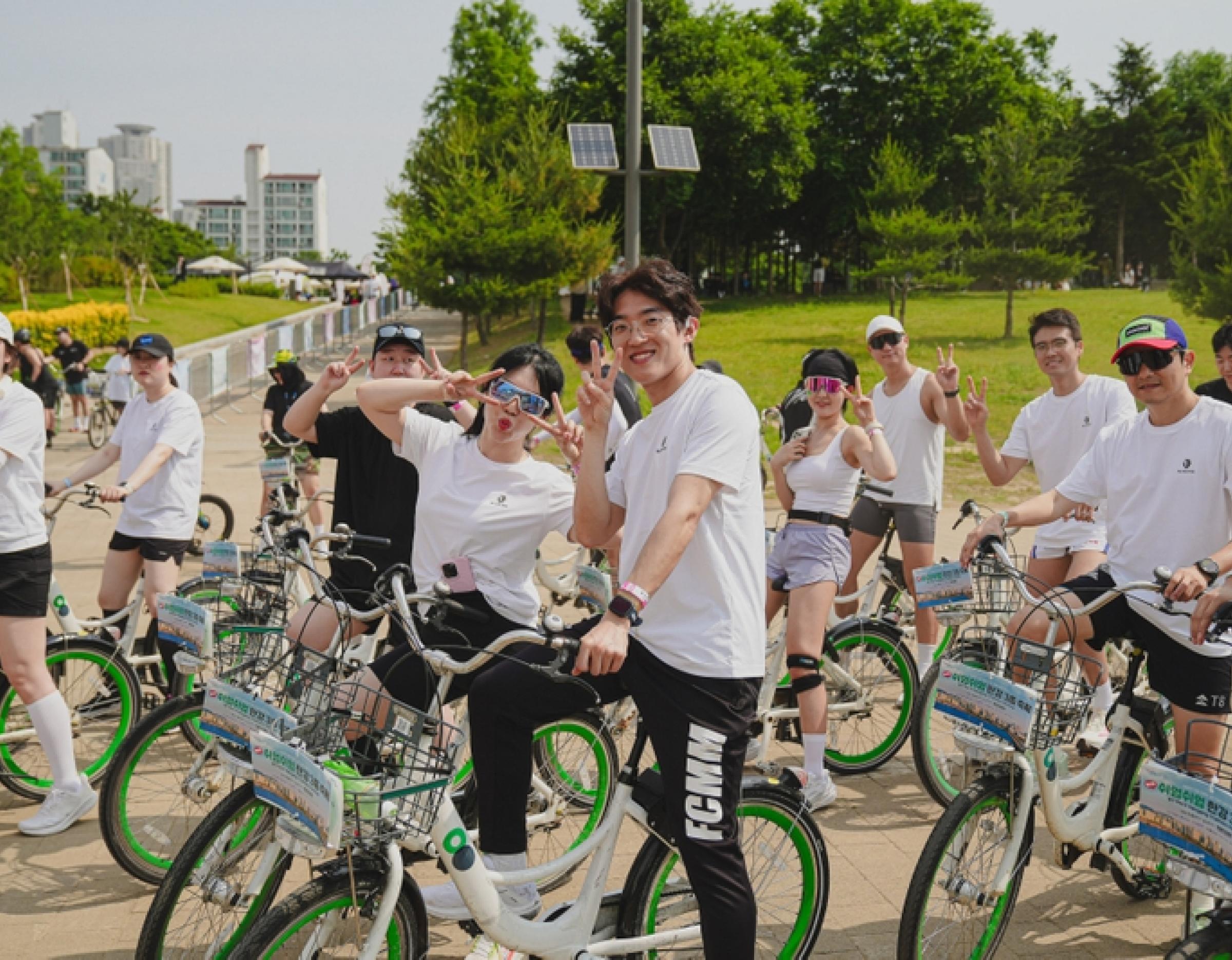 Group of smiling participants in white shirts posing with rental bikes at the Han River triathlon festival event.