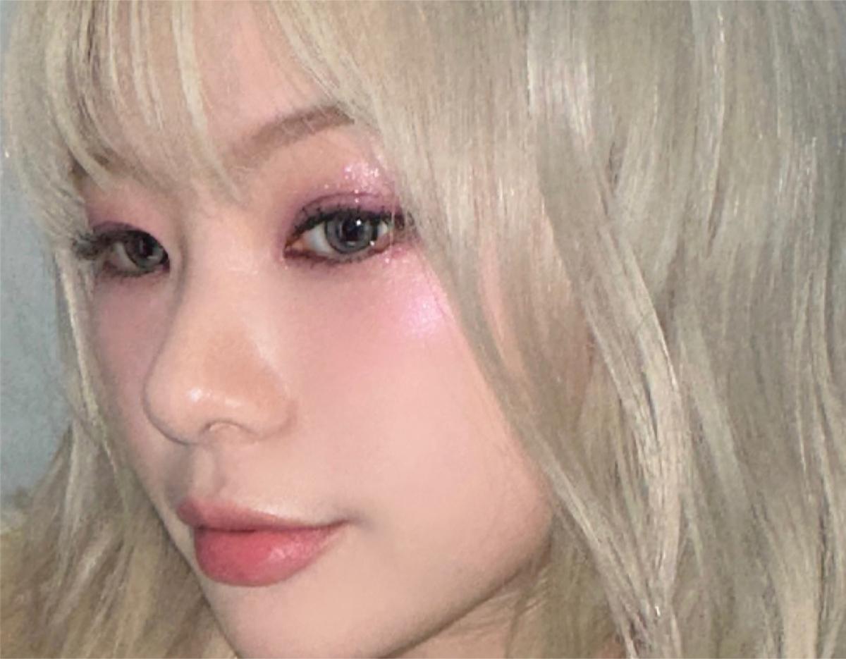 Close-up of a model with platinum blonde hair, pink glittery eye makeup, rosy cheeks, and natural pink lips