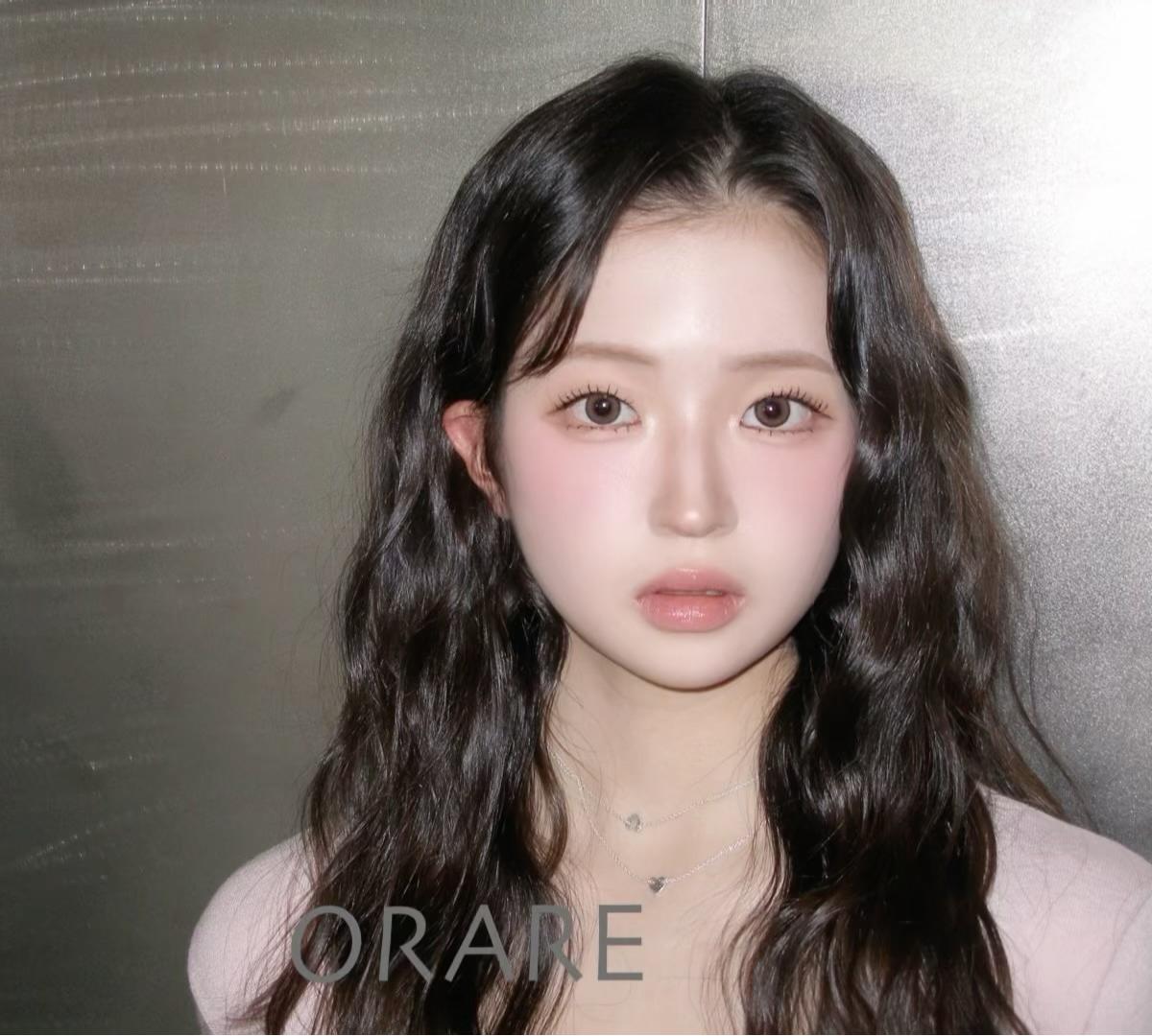 long dark wavy hair with center parting on a woman wearing layered silver necklaces and a pale pink top, salon backdrop