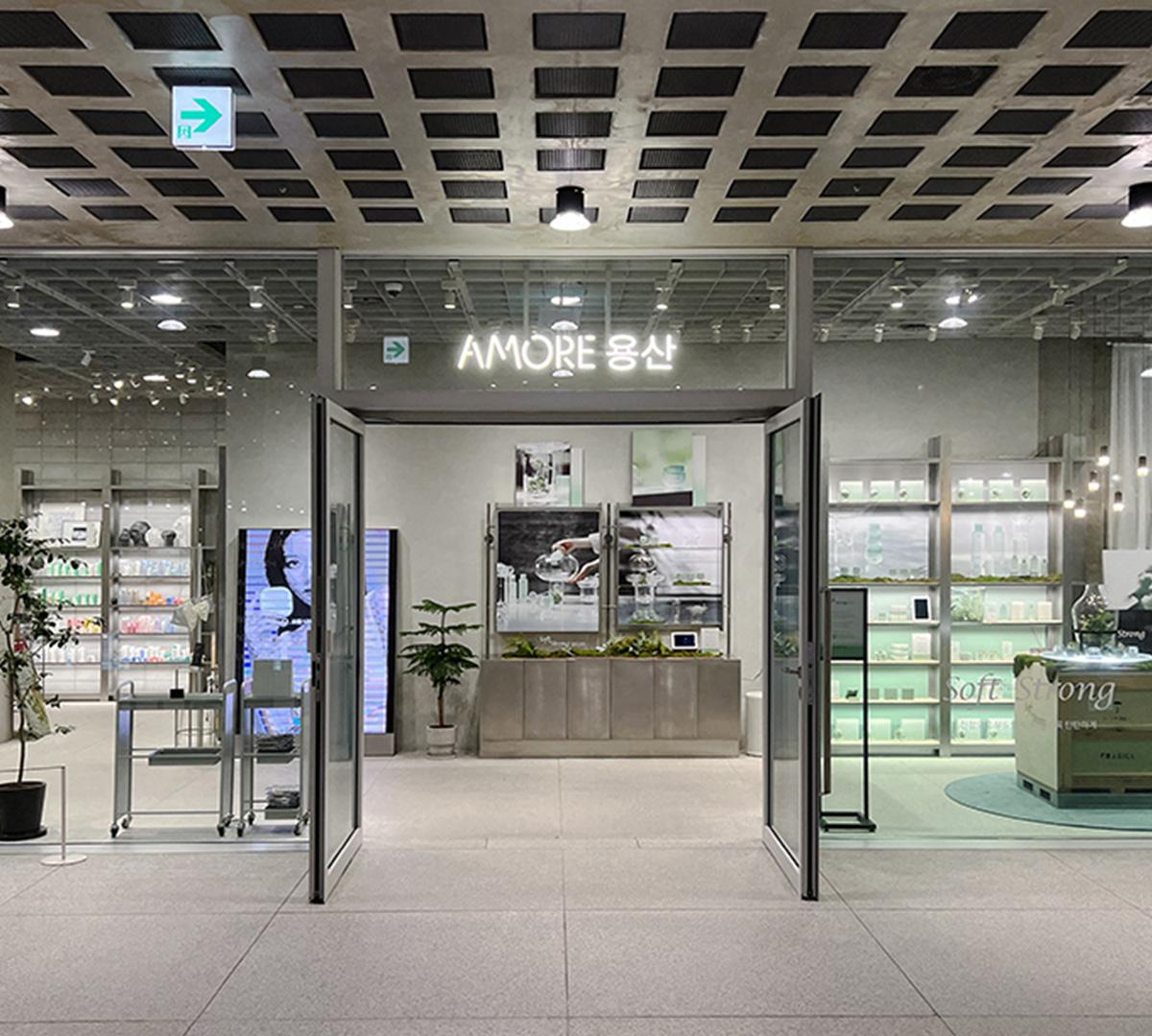 Amore Yongsan showroom entrance with glass doors, illuminated AMORE sign, product displays and minimalist interior lighting.