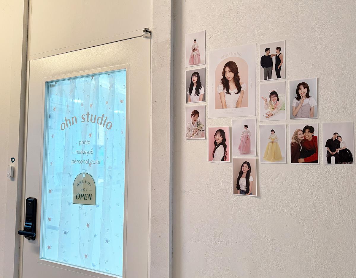 white studio door with frosted glass reading "ohn studio" and wall display of portrait photos and sample outfits