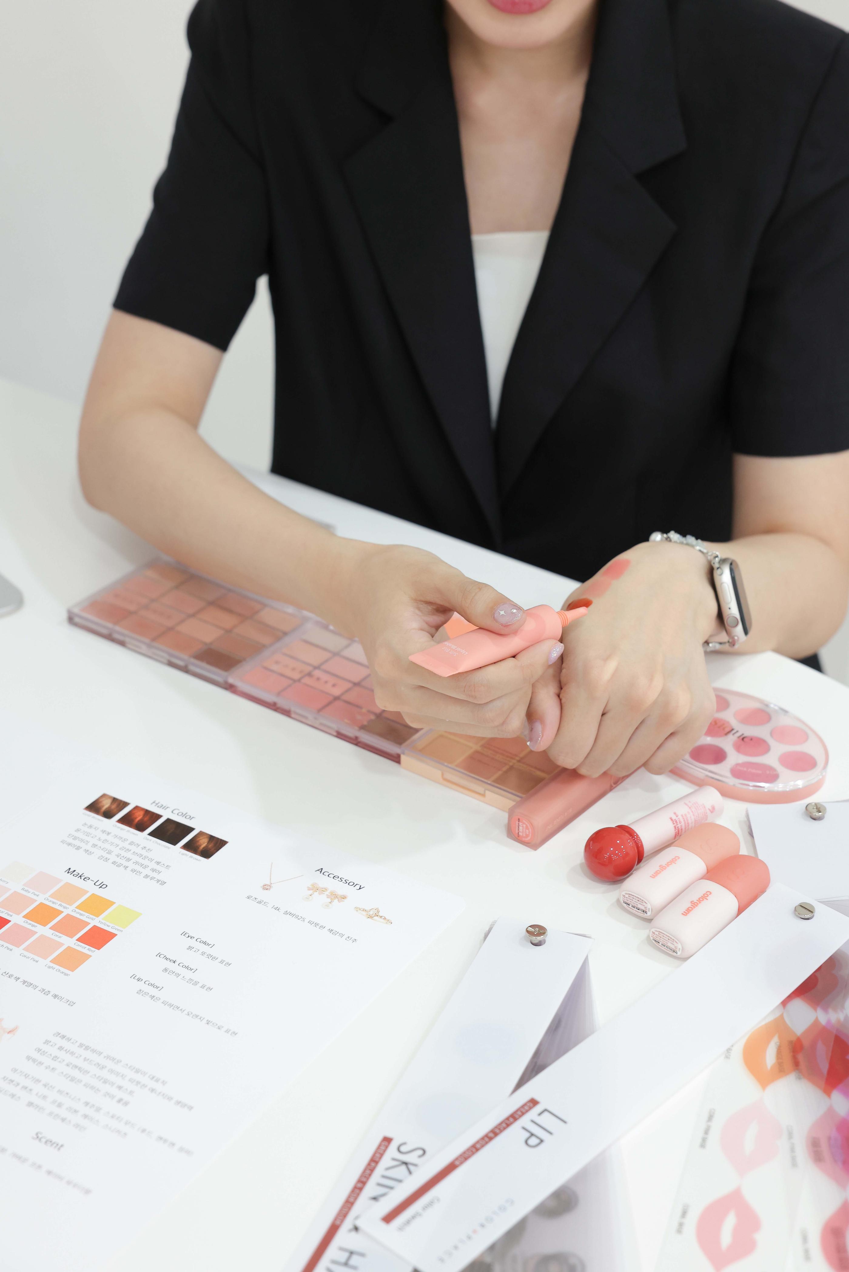 온스튜디오 컨설턴트가 손등에 립 컬러를 테스트하는 모습, 팔레트와 컬러 차트가 놓인 책상