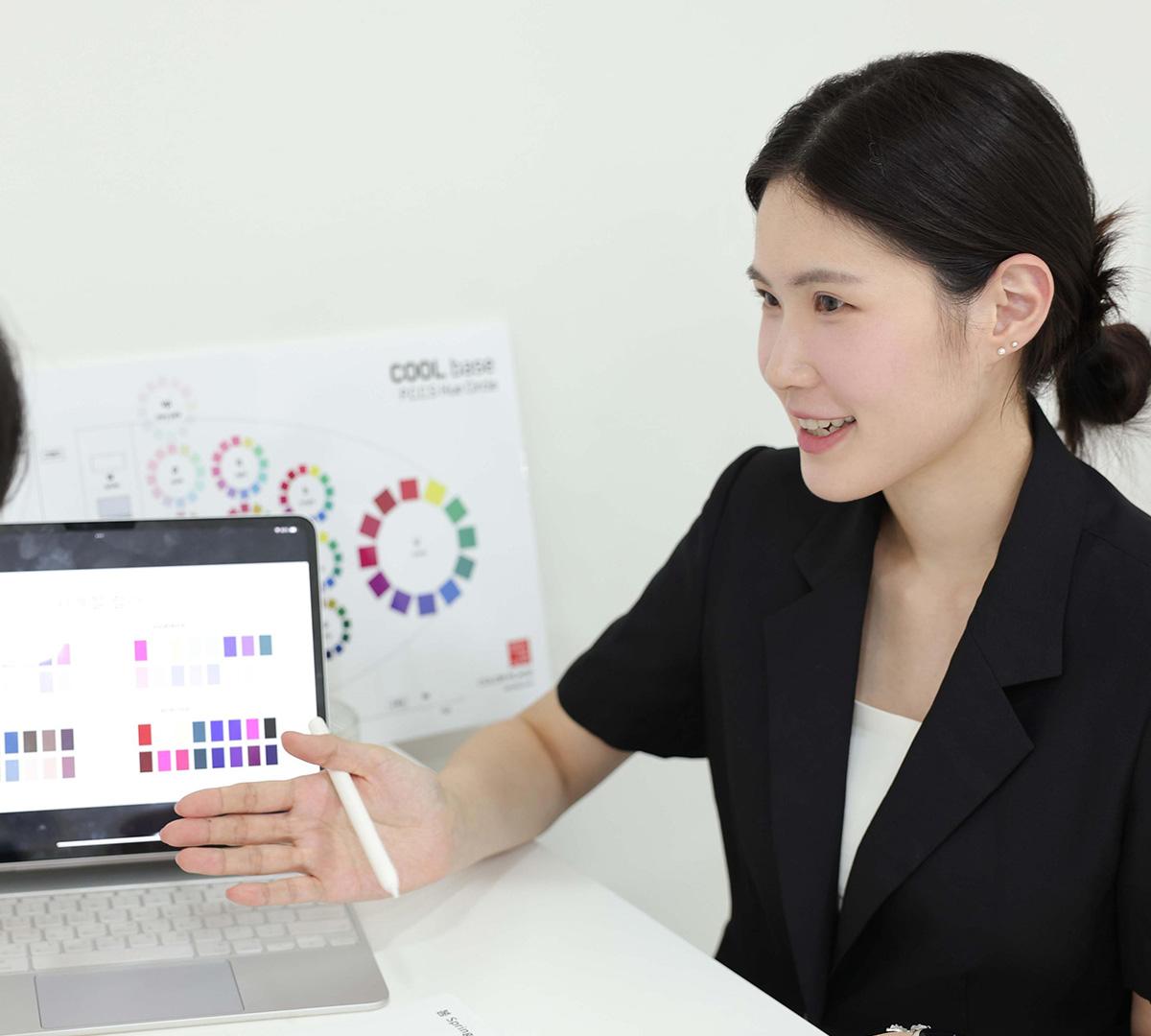 female consultant in black blazer pointing at color swatches on a laptop screen with a color wheel poster behind