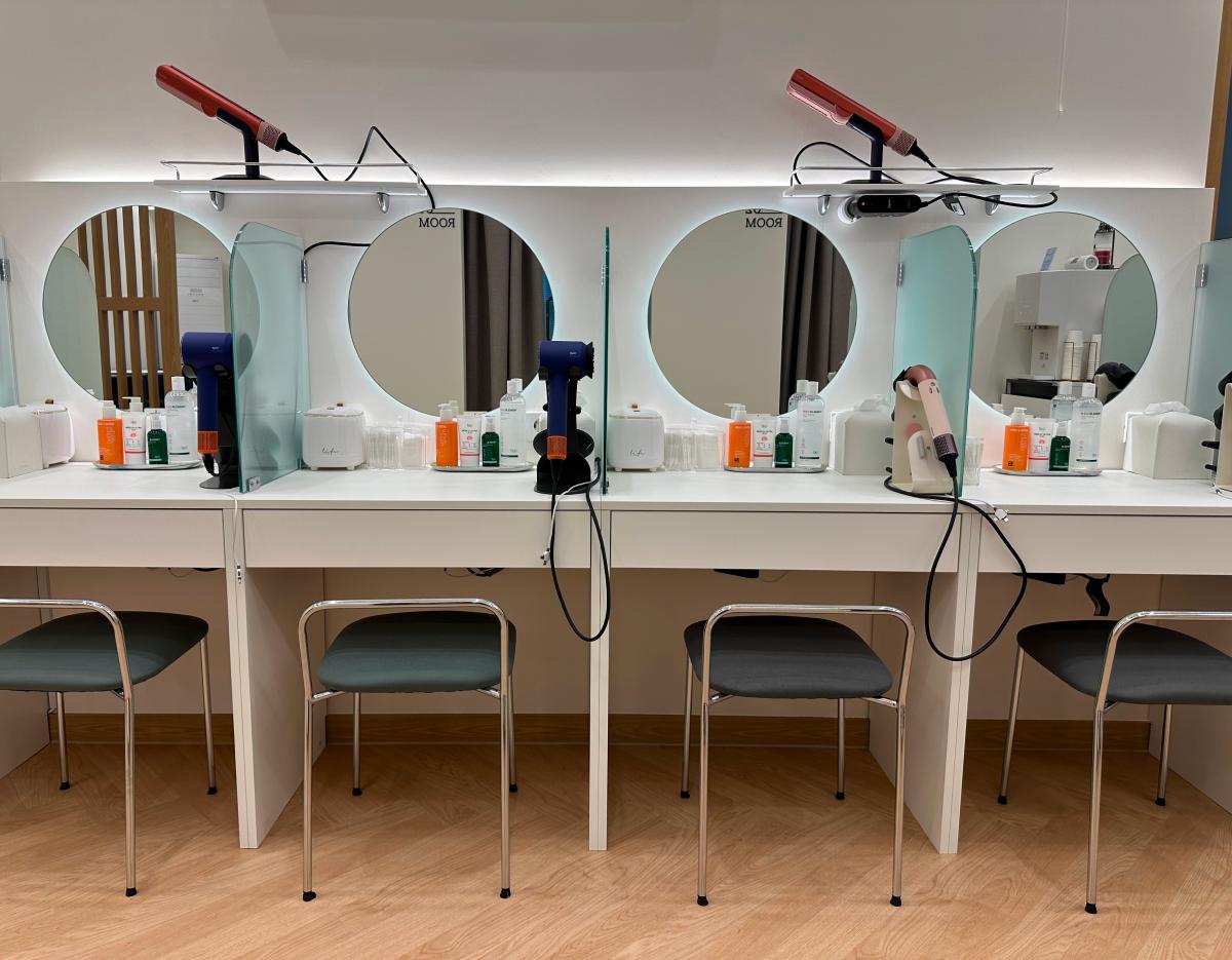 Women-only salon vanity row with round backlit mirrors, Dyson hairdryers, styling tools, and chairs in private cubicles