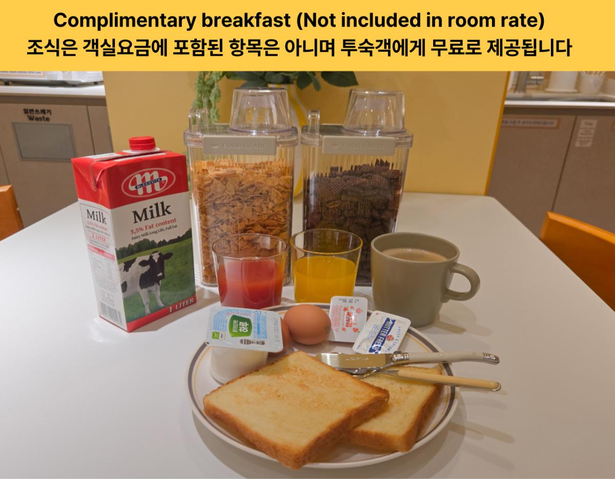 桌上擺放免費早餐：兩片烤吐司、雞蛋、果醬、奶油、牛奶盒、玉米片及巧克力穀物罐、果汁與熱咖啡杯。