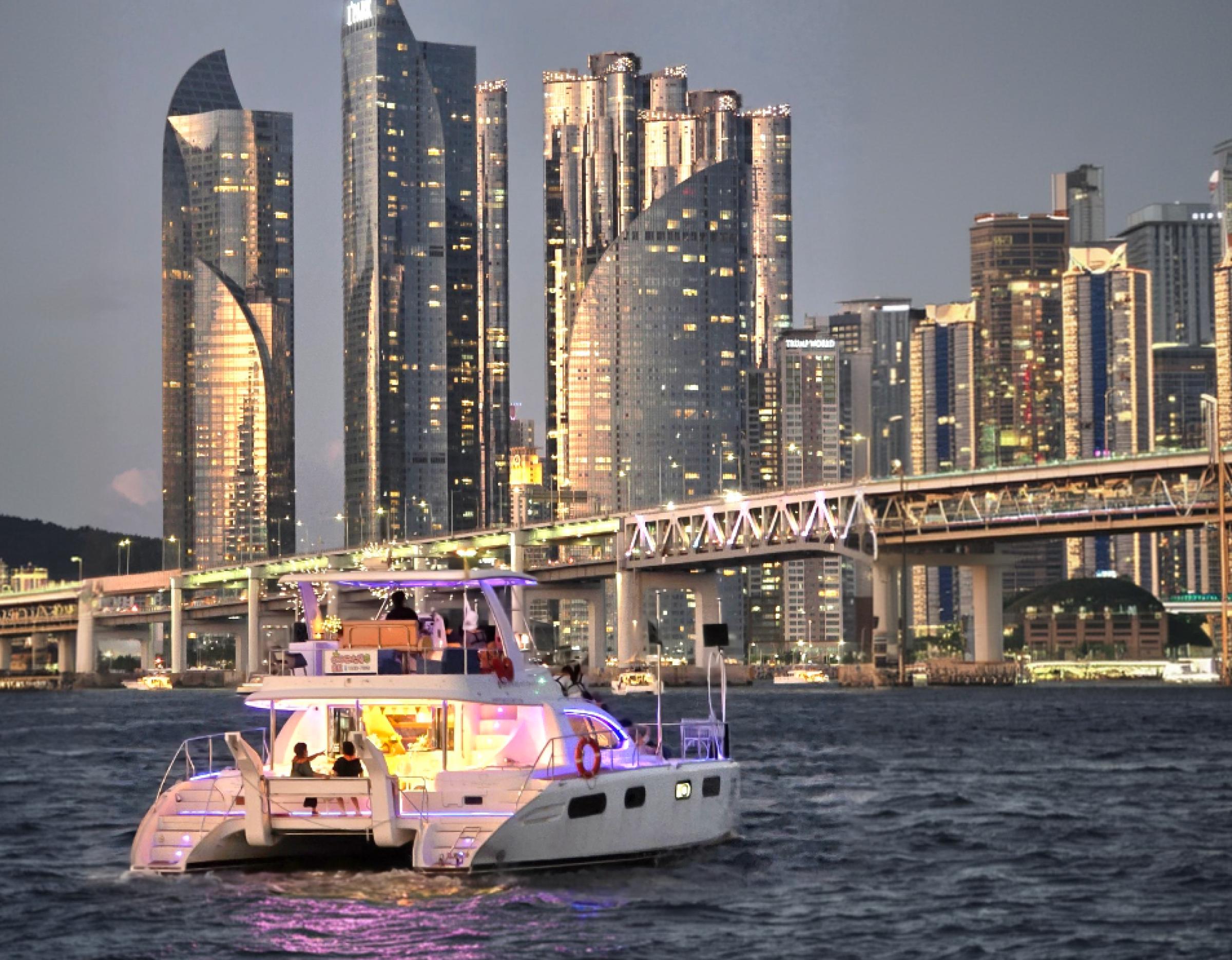 illuminated private yacht at dusk on water with Busan skyline and Gwangan Bridge in background