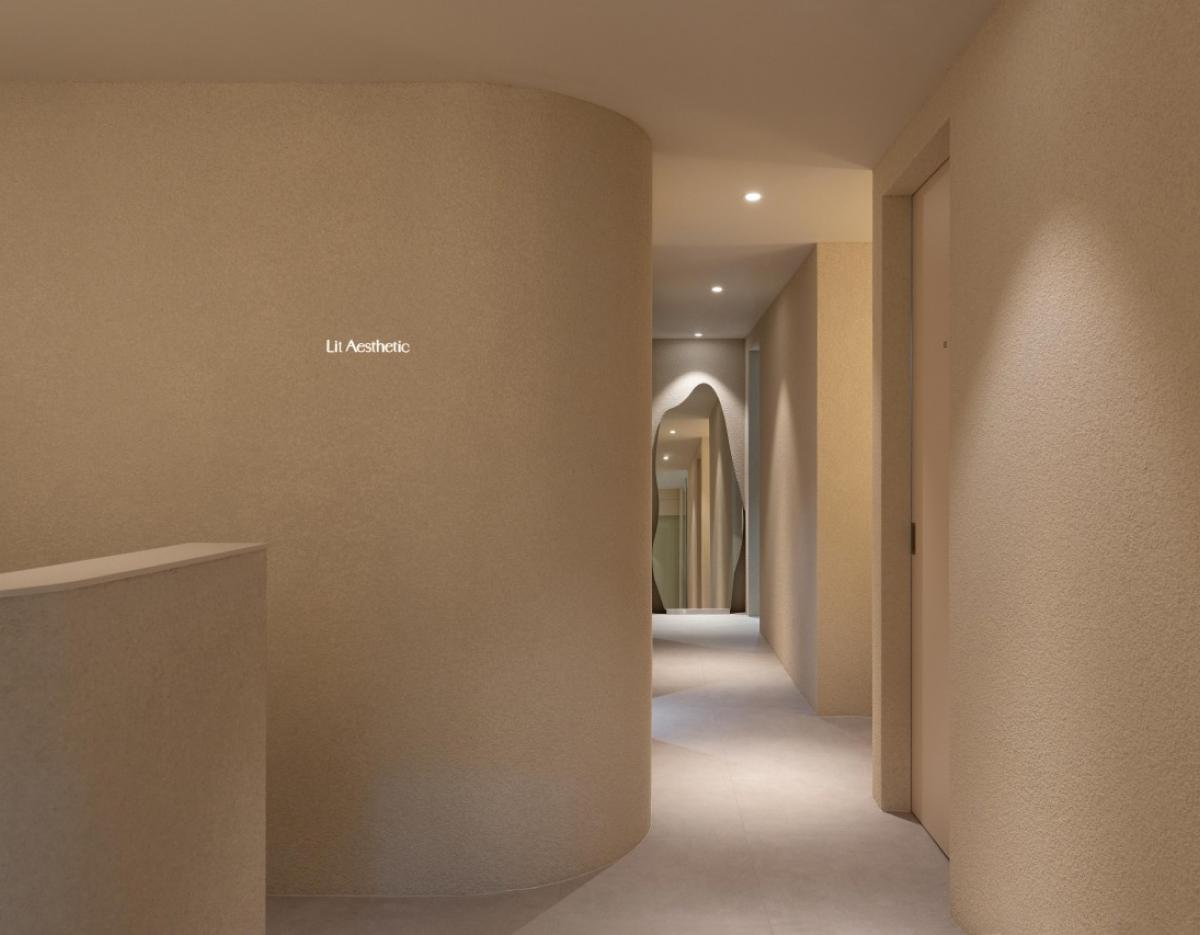 Minimalist beige hallway with curved textured walls, recessed ceiling lights and an arched mirror at the corridor end