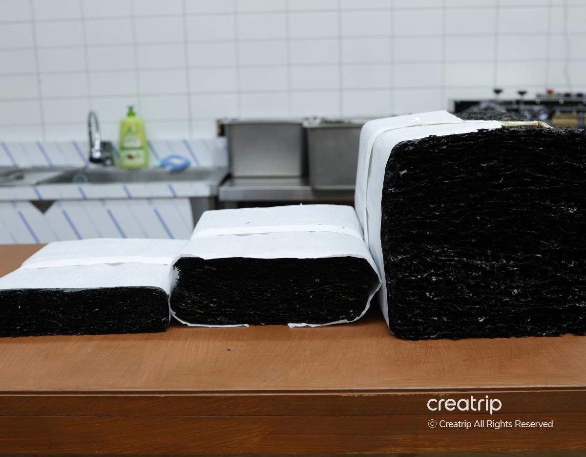 Stacks of dark roasted seaweed sheets wrapped in white paper on a wooden counter at 가원옥돌김 명동 restaurant kitchen