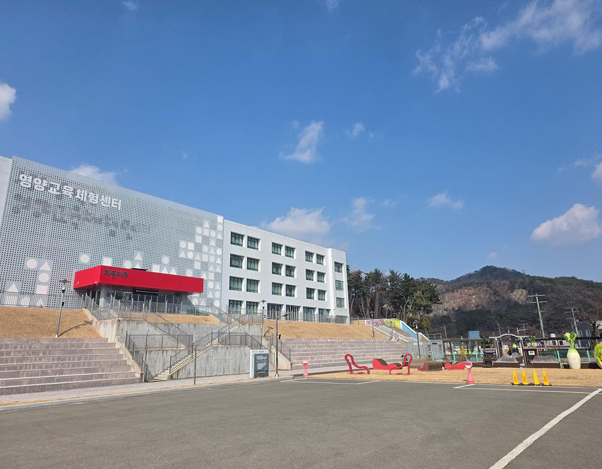 Modern white civic building with red canopy, terraced concrete steps and empty plaza under a clear blue sky in Busan