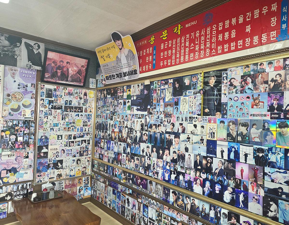 wall covered with hundreds of BTS photo cards, posters, and fan images inside a Busan ARMY-themed restaurant corner