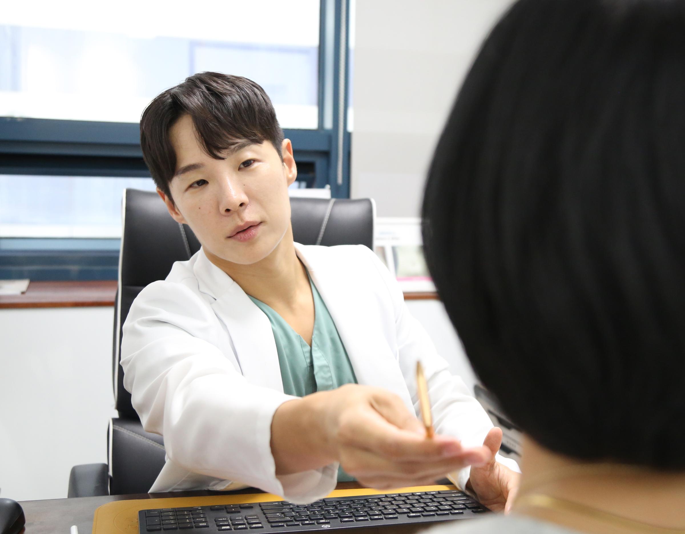 Doctor in white coat seated at desk handing a pen to a patient across from them in a consultation room