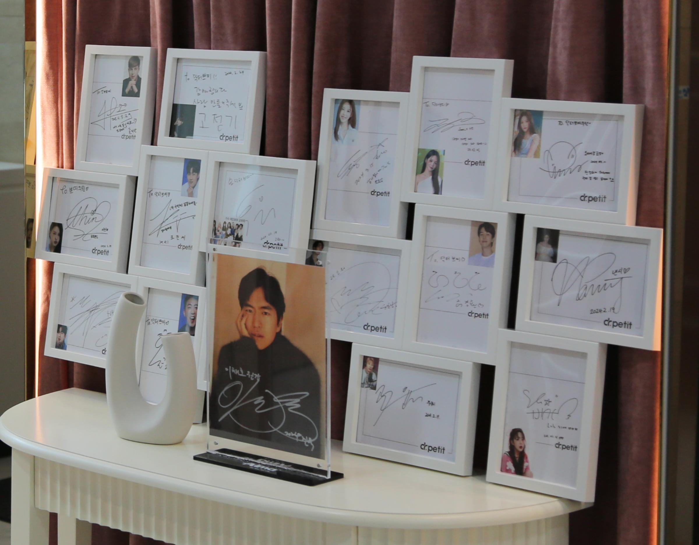 wall of white framed celebrity autograph photos and signed headshot plaques displayed on a curved white table of Dr.petit clinic