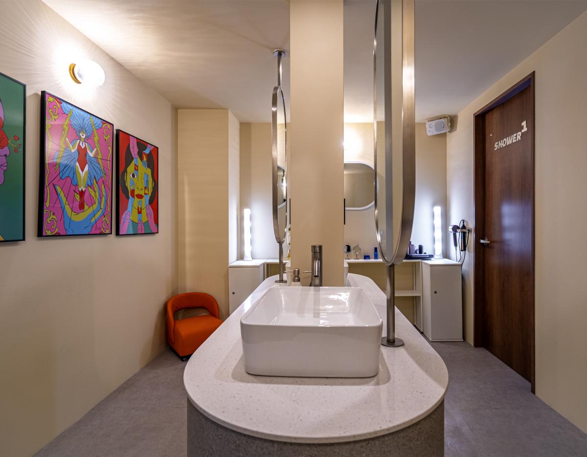communal washbasin island with round mirrors, colorful pop-art on wall and a door labeled "SHOWER 1" in transit lounge