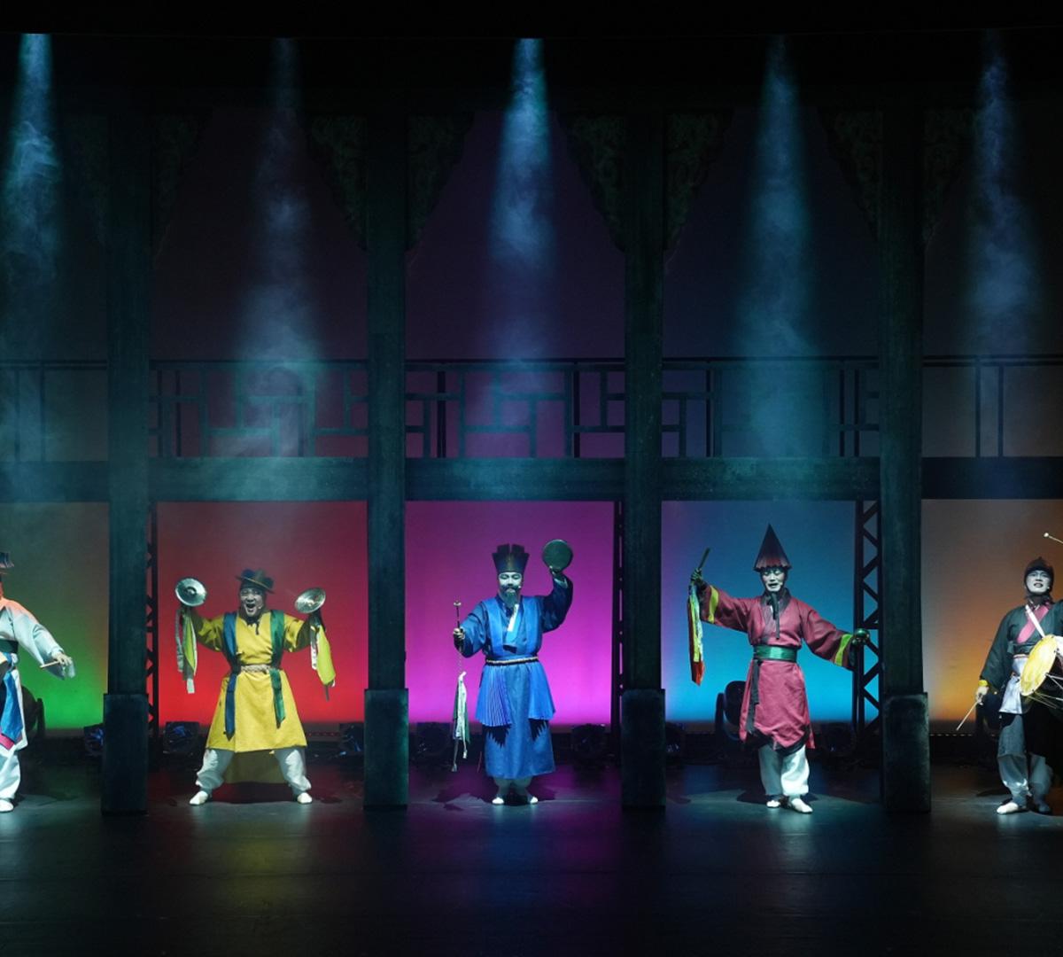 Traditional Korean performers in colorful hanbok and masks on stage at Seoul National Jeongdong Theater, lit by spotlights